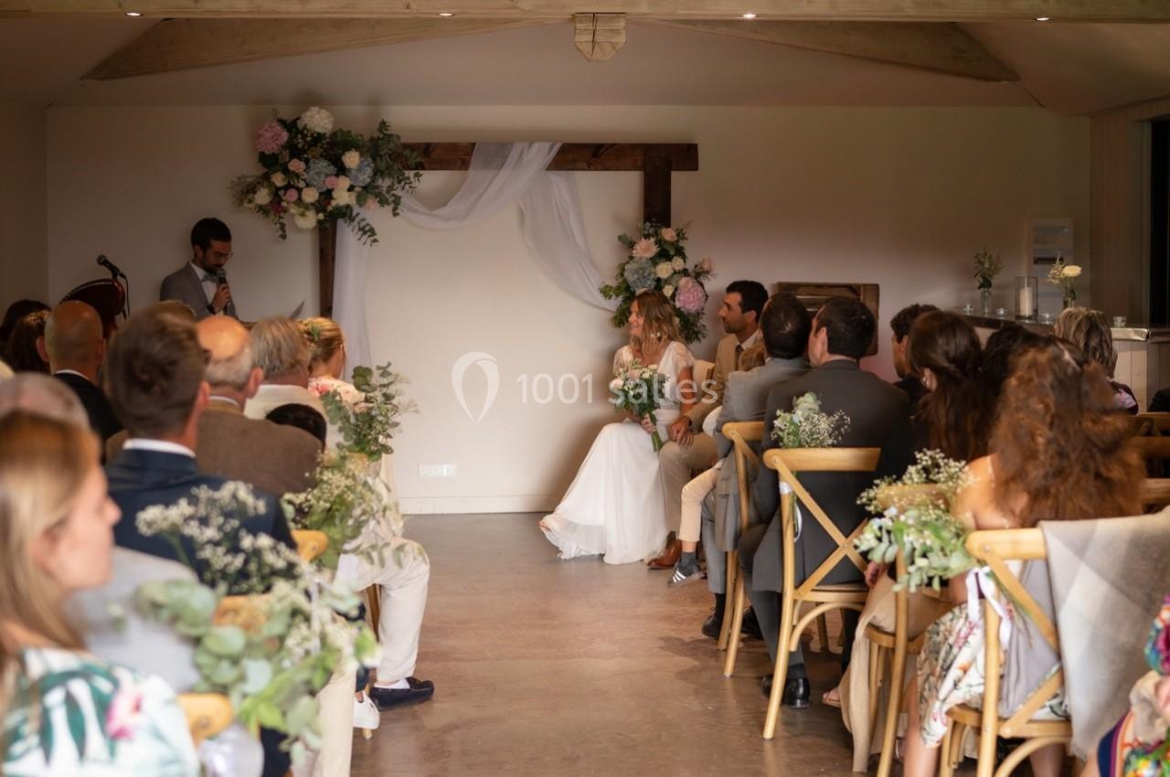 Cérémonie de mariage en intérieur avec des invités assis, un couple au centre et un officiant en train de parler.