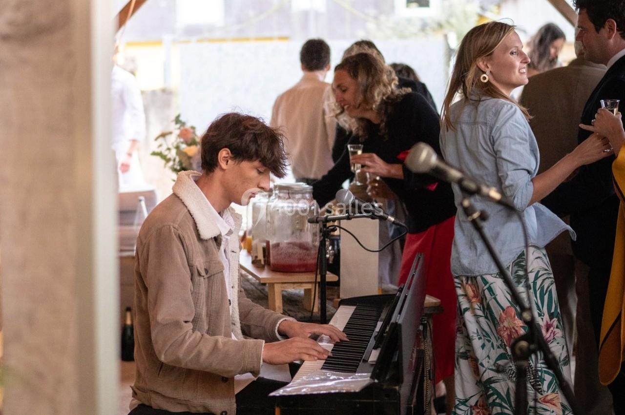 Un homme joue du piano électrique lors d'un événement convivial avec des invités en arrière-plan.