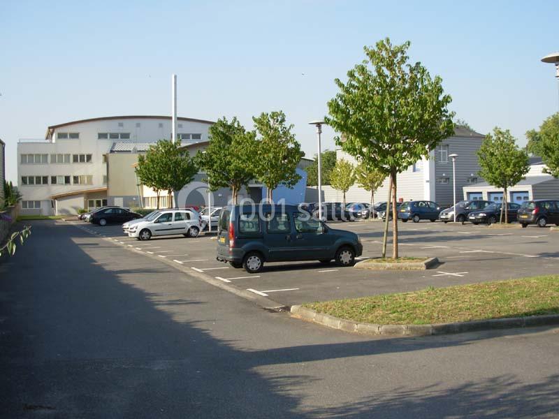 Parking extérieur avec quelques voitures stationnées, entouré de bâtiments modernes et d'arbres alignés.