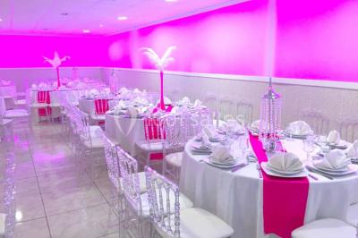 Salle de réception décorée avec des tables rondes, nappes blanches, chaises transparentes et centres de table fleuris.