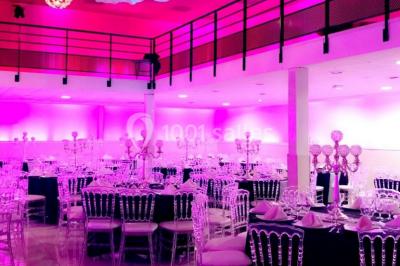 Salle de réception décorée avec des tables rondes, nappes blanches, chaises transparentes et centres de table fleuris.