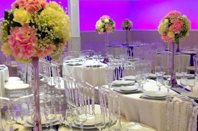 Salle de réception décorée avec des tables rondes, nappes blanches, chaises transparentes et centres de table fleuris.