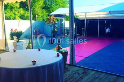 Salle de réception décorée avec des tables rondes, nappes blanches, chaises transparentes et centres de table fleuris.