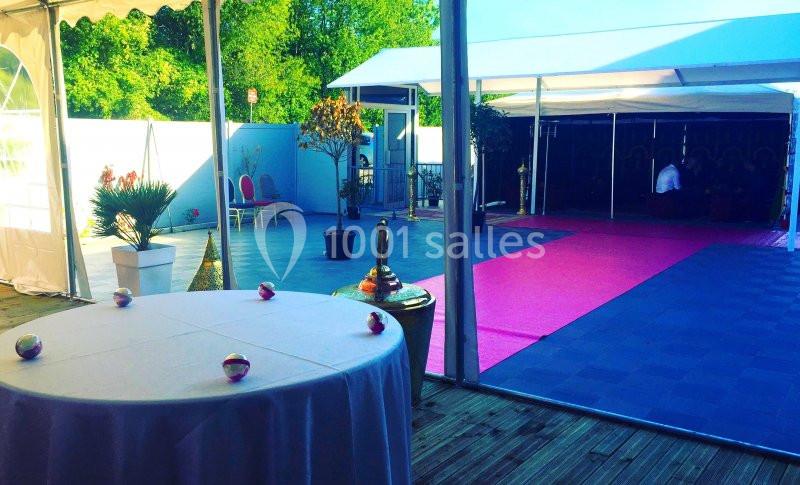 Espace extérieur aménagé avec tapis roses, chaises et tables sous des tentes, entouré de verdure.
