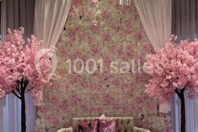 Salle de réception décorée avec des tables rondes, nappes blanches, chaises transparentes et centres de table fleuris.