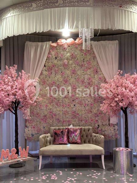 Mur floral rose et blanc avec canapé beige, coussins décoratifs et arbres roses dans un décor élégant.