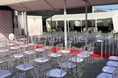 Salle de réception décorée avec des tables rondes, nappes blanches, chaises transparentes et centres de table fleuris.