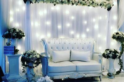 Salle de réception décorée avec des tables rondes, nappes blanches, chaises transparentes et centres de table fleuris.