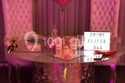 Salle de réception décorée avec des tables rondes, nappes blanches, chaises transparentes et centres de table fleuris.