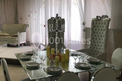 Salle de réception décorée avec des tables rondes, nappes blanches, chaises transparentes et centres de table fleuris.