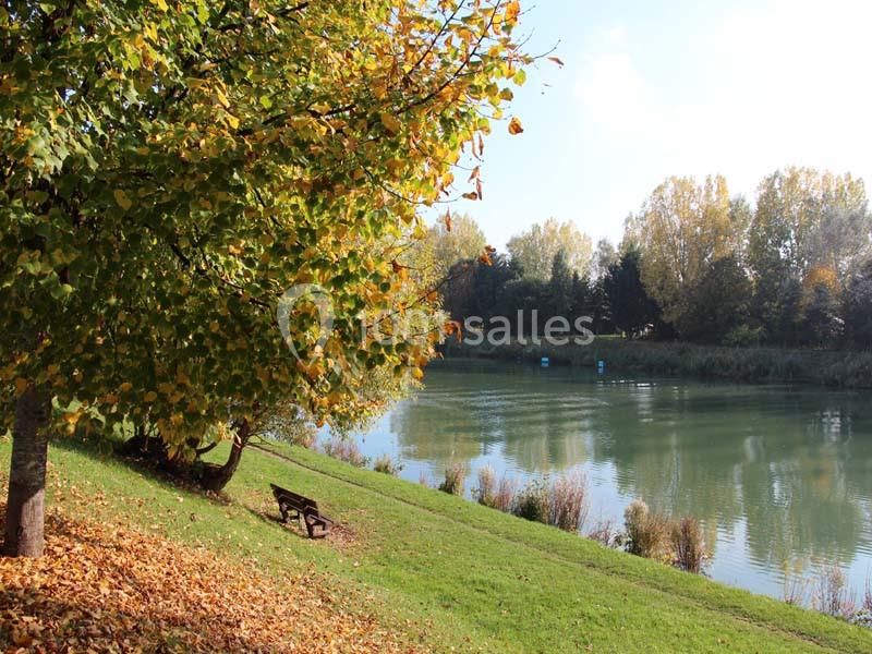 Banc en bois sous un arbre aux feuilles jaunies, près d'une rivière bordée de végétation en automne.