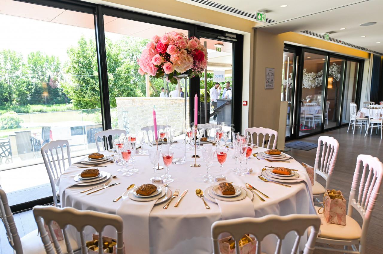 Table élégamment dressée avec nappes blanches, vaisselle dorée, verres à pied et centre de table floral rose.