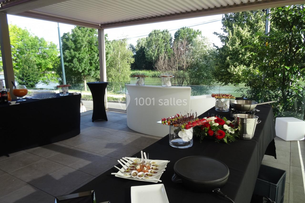 Table de buffet dressée avec des amuse-bouches, fleurs rouges et vue sur un espace extérieur verdoyant.