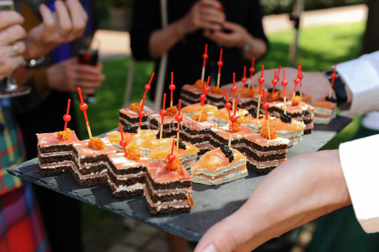 Plateau de canapés variés avec des brochettes rouges, tenu par une personne lors d'un événement en extérieur.