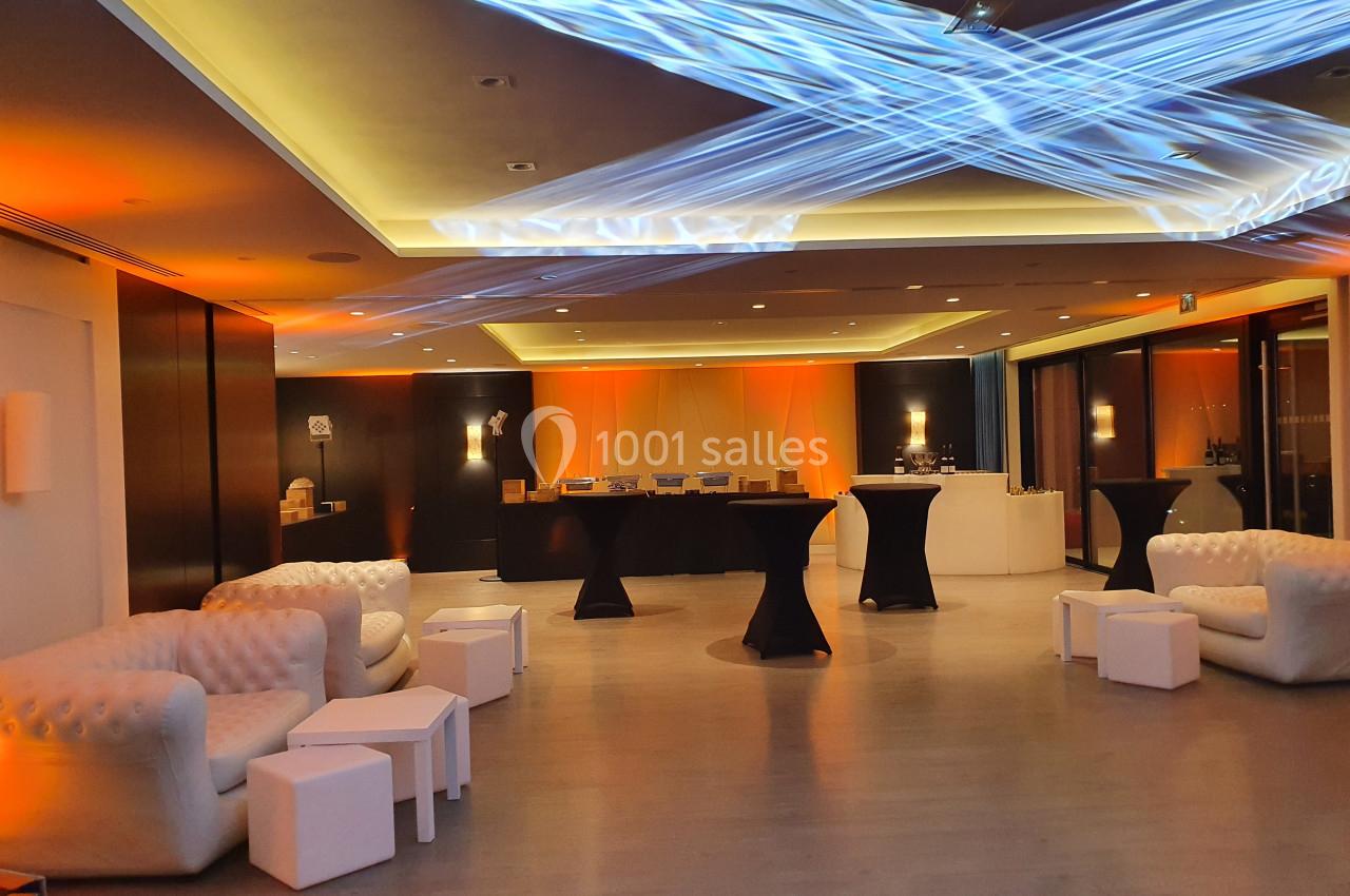Salle moderne avec canapés blancs, tables basses et buffet éclairé par des lumières orange et bleues.