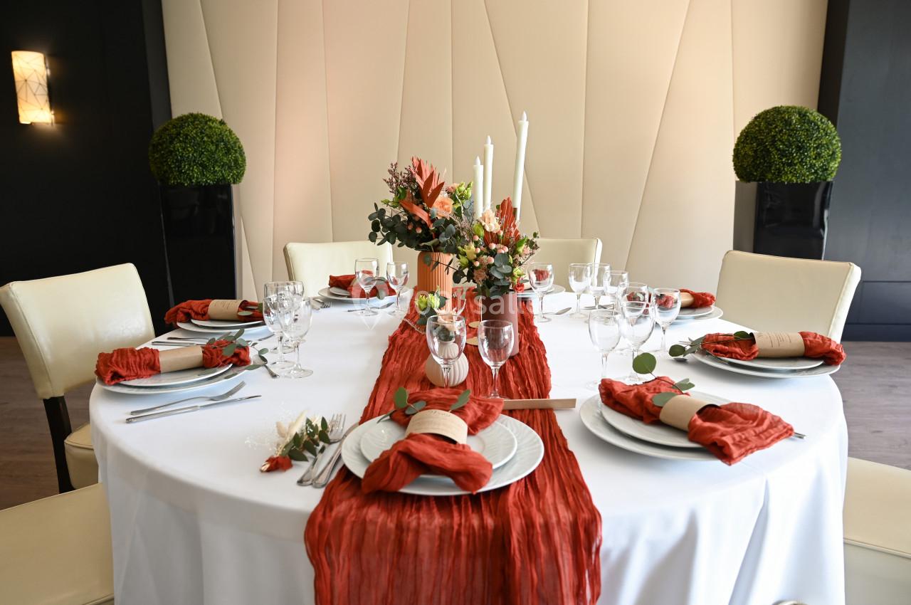 Table ronde décorée avec une nappe blanche, des serviettes rouges, un chemin de table assorti et un centre floral.