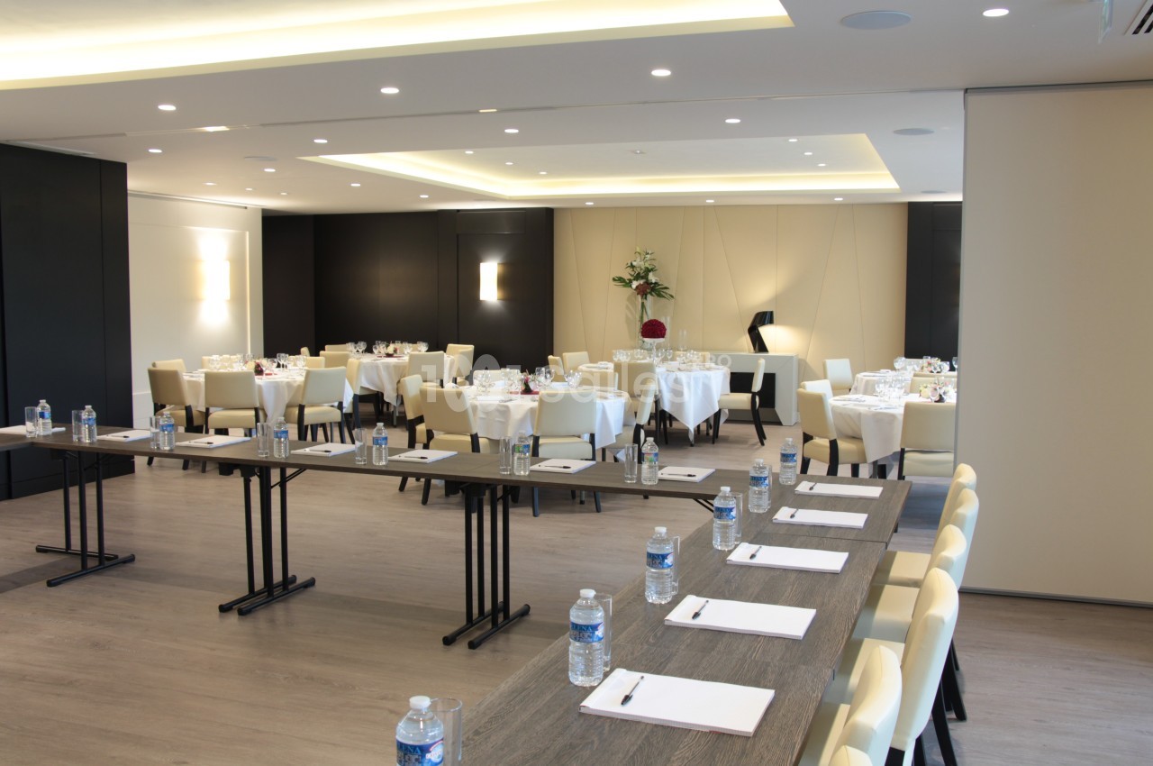 Salle de réunion lumineuse aménagée avec des tables, des chaises, des bouteilles d'eau et des blocs-notes.