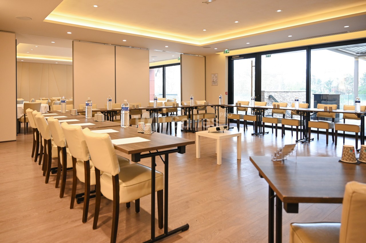 Salle de réunion lumineuse avec tables disposées en U, chaises beige, bouteilles d'eau et blocs-notes sur les tables.