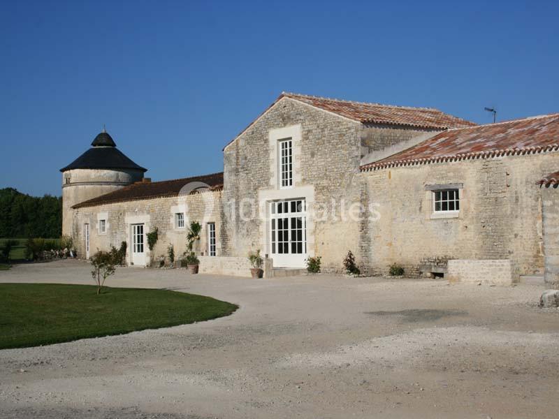 Bâtiment en pierre avec toit en tuiles, entouré de végétation, sous un ciel bleu clair.