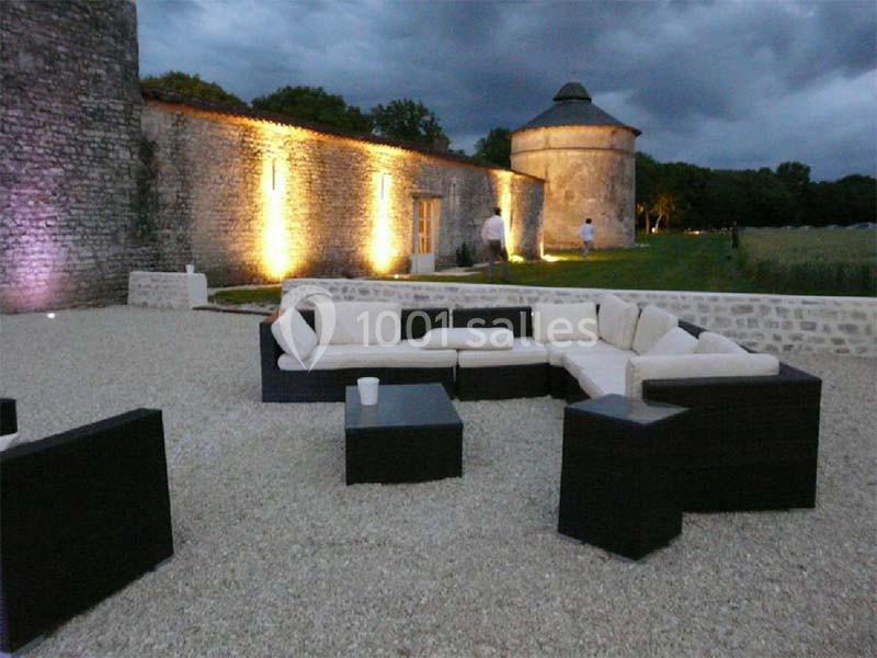 Mobilier de jardin moderne avec canapés et tables basses sur une terrasse en gravier, près d'un mur en pierre éclairé.