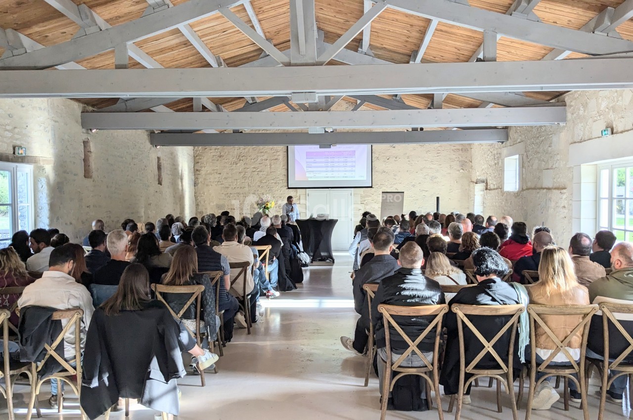 Salle en pierre avec des poutres apparentes, des personnes assises assistent à une présentation projetée sur un écran.