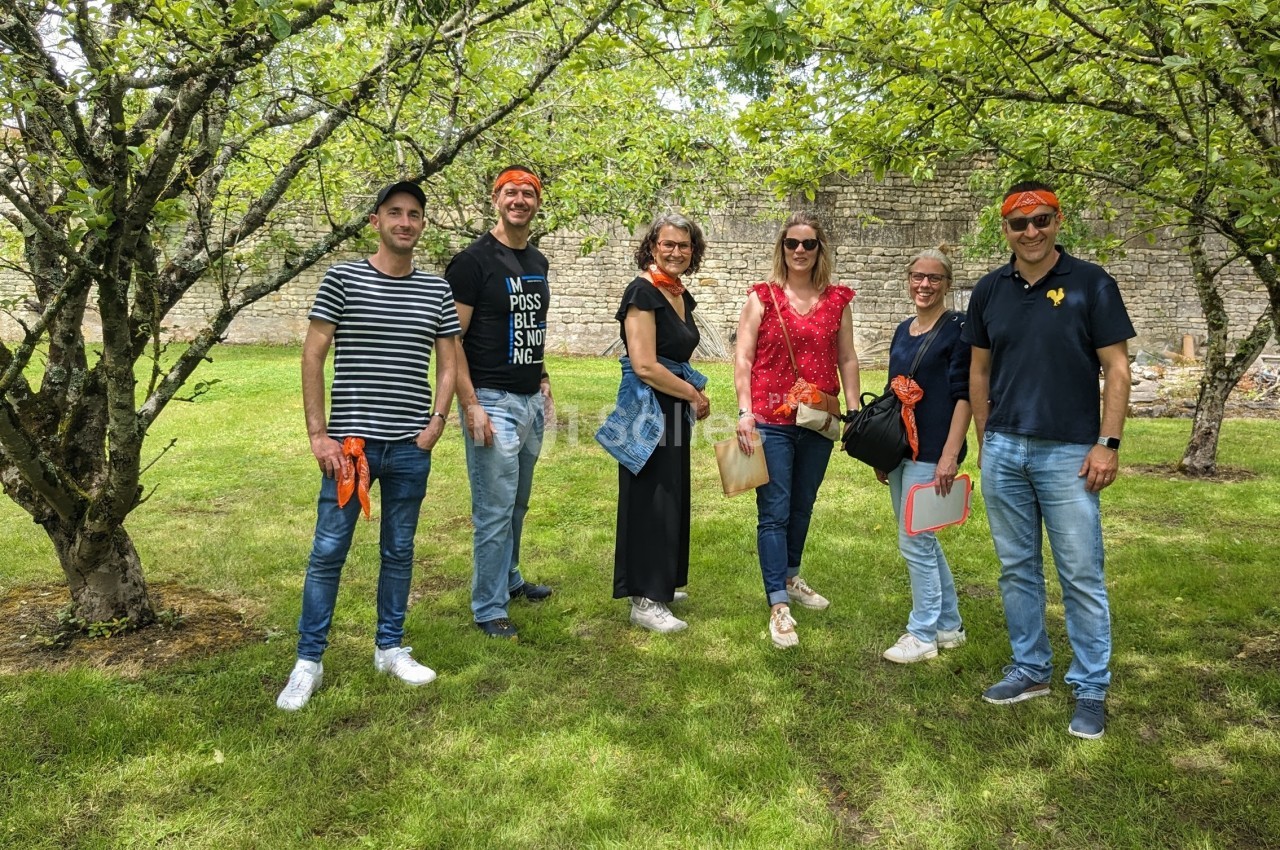 Un groupe de six personnes posant dans un jardin verdoyant avec des arbres et un mur en pierre en arrière-plan.