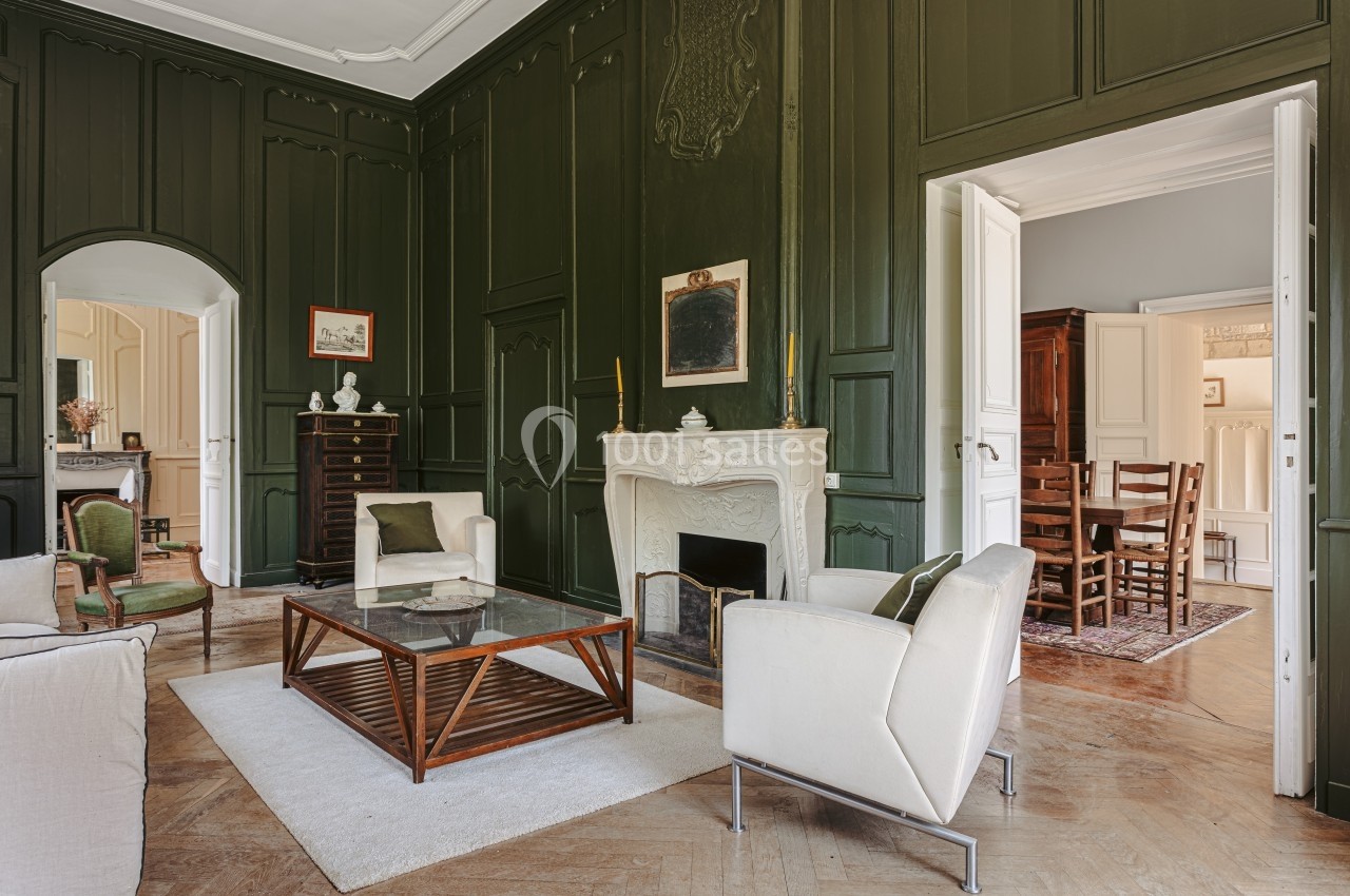 Salon élégant avec murs vert foncé, cheminée blanche sculptée, mobilier moderne et parquet en bois.