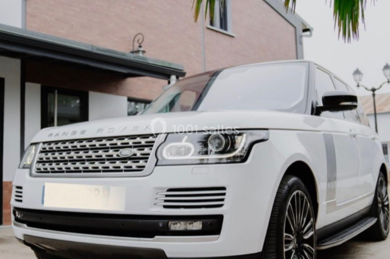 SUV blanc garé devant une maison en briques avec des fenêtres et un palmier au premier plan.