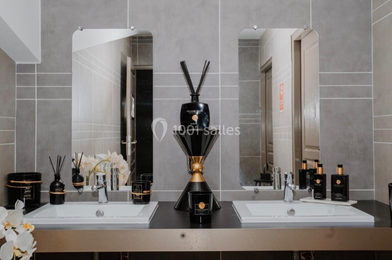 Deux lavabos avec miroirs, ornés de produits de soin et de décoration, dans une salle de bain moderne aux tons neutres.