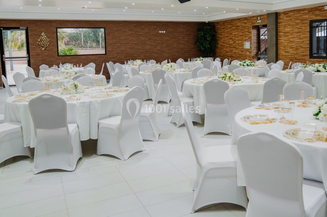 Salle de réception avec tables rondes dressées de nappes blanches, chaises assorties et décorations florales.