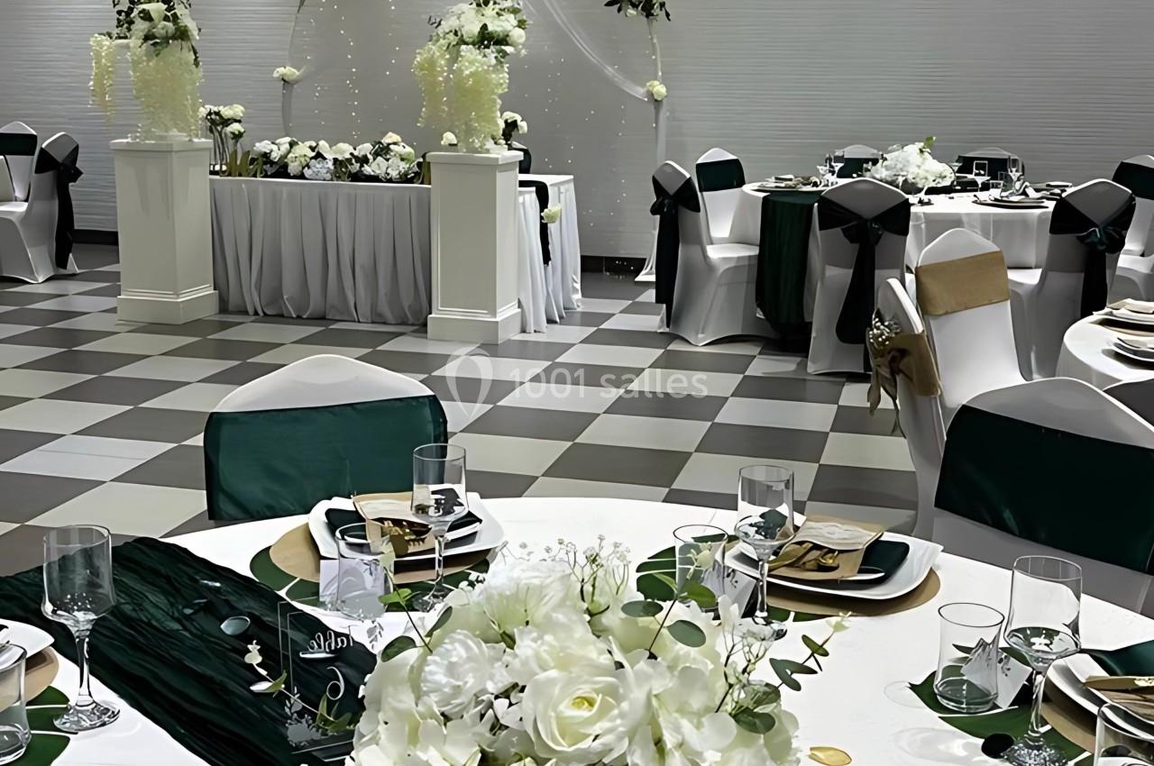 Salle de réception décorée avec des tables rondes, nappes vertes et blanches, et des arrangements floraux élégants.