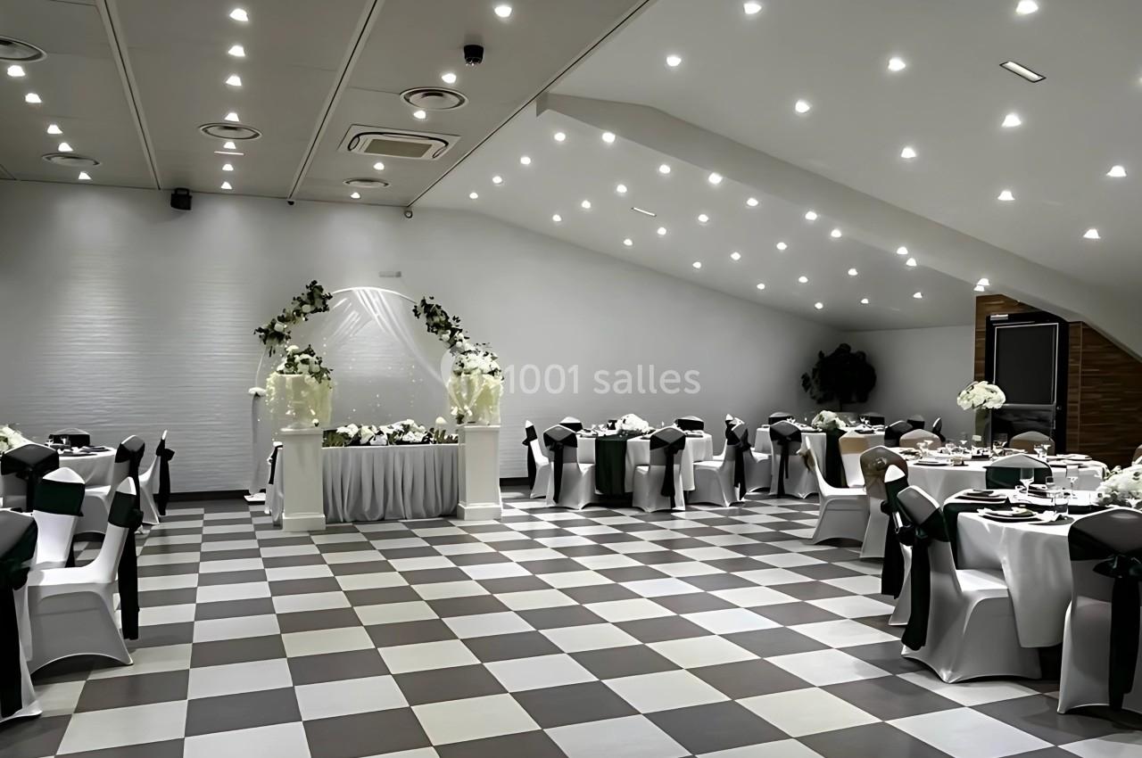 Salle de réception élégante avec tables rondes décorées de nappes blanches et un arche floral au centre.