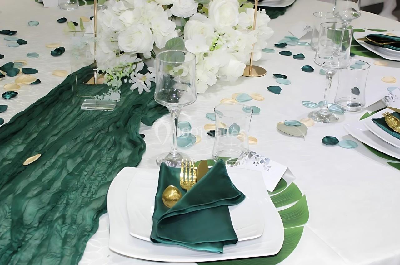 Table décorée avec une nappe blanche, un chemin de table vert, des pétales colorés et une vaisselle élégante.