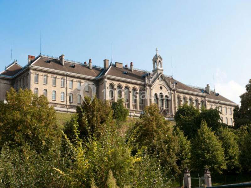 Bâtiment ancien en pierre avec des fenêtres cintrées, entouré d'arbres et sous un ciel dégagé.