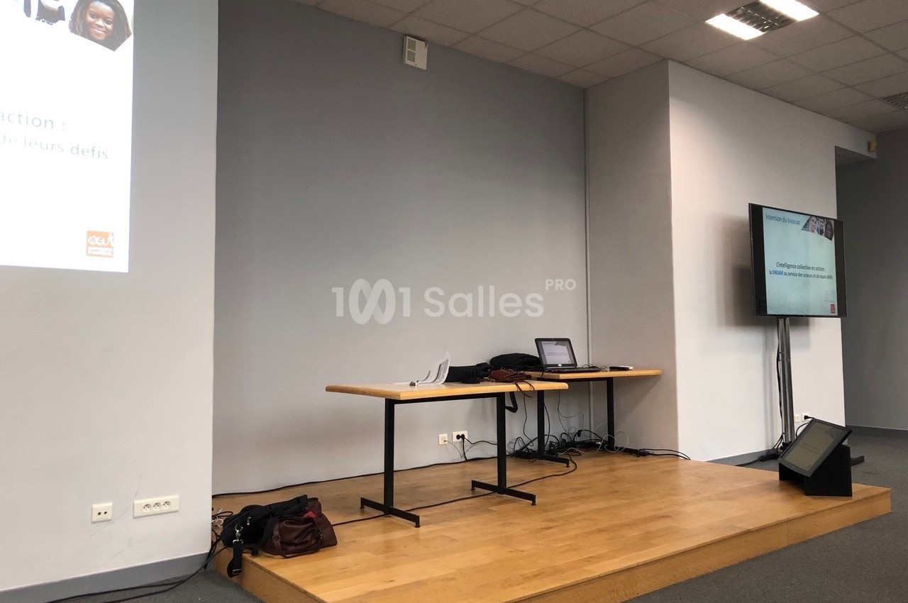 Salle de conférence avec une estrade, un écran de projection, un ordinateur portable et un écran secondaire.