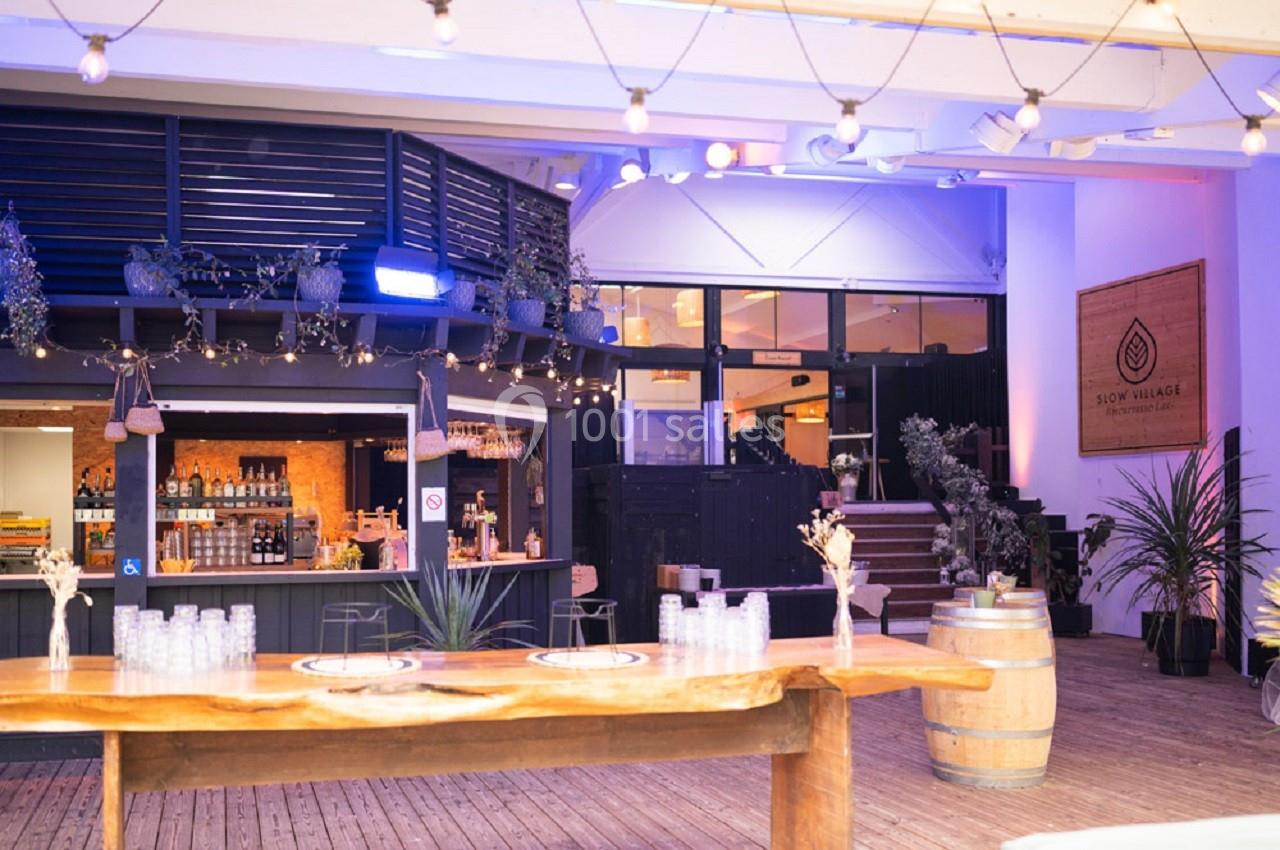 Espace intérieur décoré avec un bar en bois, des plantes suspendues, des lumières tamisées et des tables en bois.