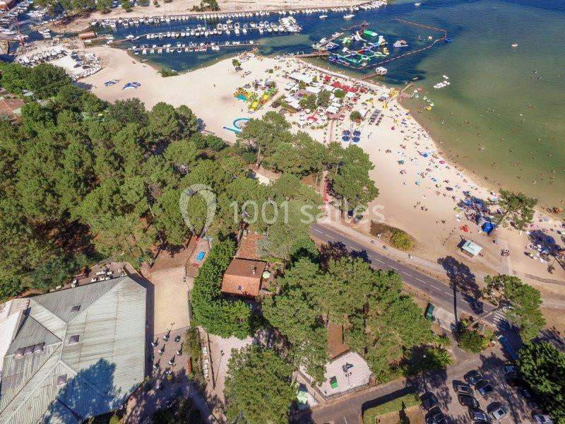Vue aérienne d'une plage animée avec des installations de loisirs, des arbres et un port de plaisance à proximité.