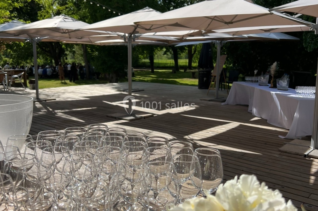 Verres vides alignés sur une table en bois, avec des fleurs blanches au premier plan et des parasols dans un jardin en…