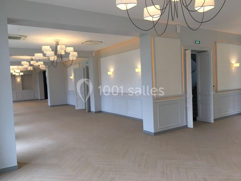 Salle lumineuse avec parquet clair, murs blancs et gris, éclairée par des lustres modernes et appliques murales.