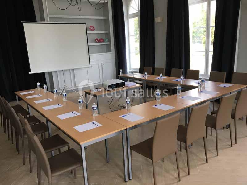 Salle de réunion avec tables disposées en U, chaises, écran de projection, bouteilles d'eau et blocs-notes.