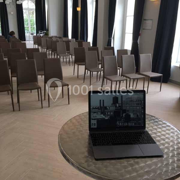 Salle de conférence lumineuse avec des rangées de chaises vides et un ordinateur portable posé sur une table ronde au…