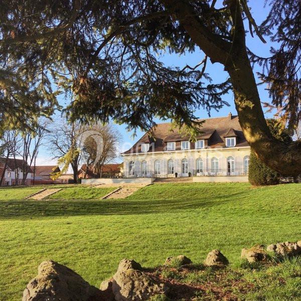 Bâtiment en pierre avec toit en ardoise, entouré d'un parc verdoyant sous un ciel dégagé.