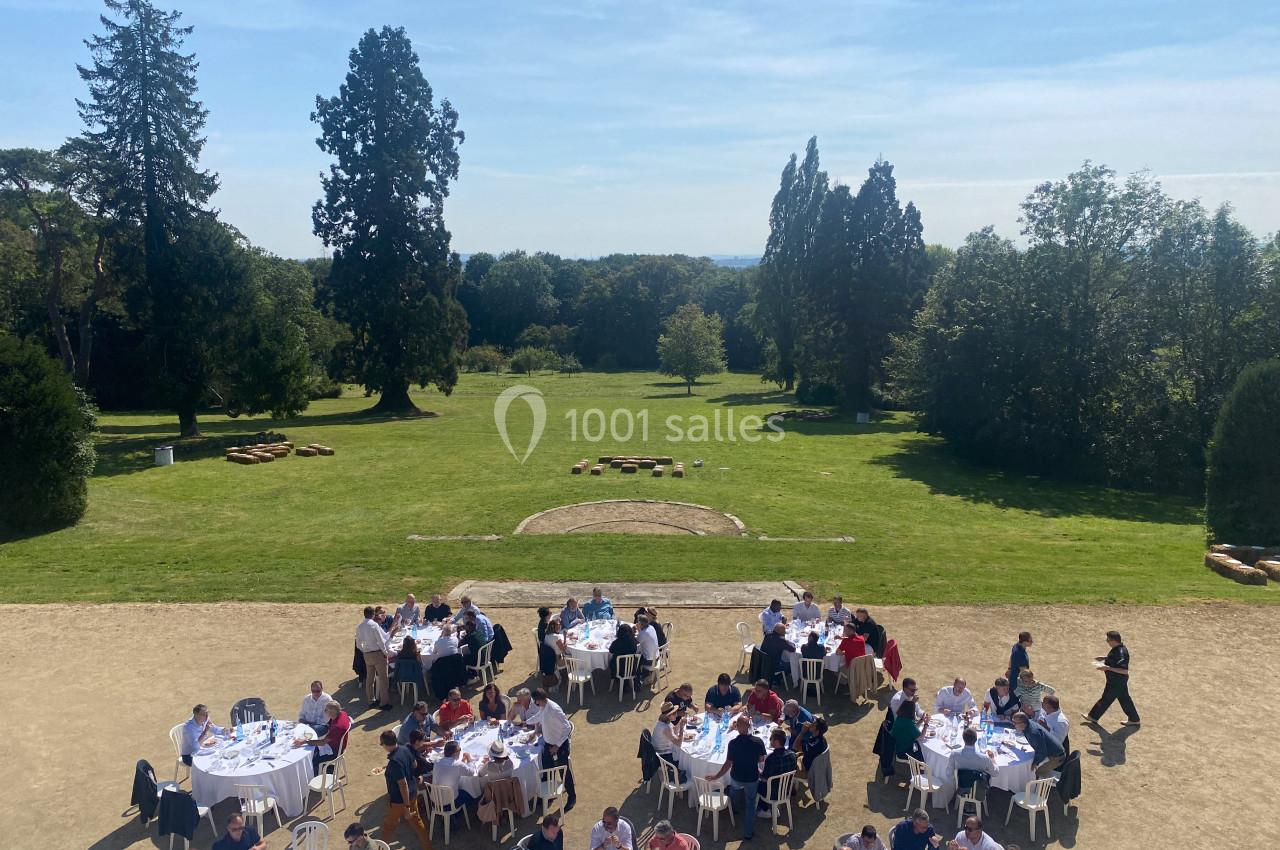 Personnes assises à des tables rondes en plein air dans un parc verdoyant sous un ciel dégagé.