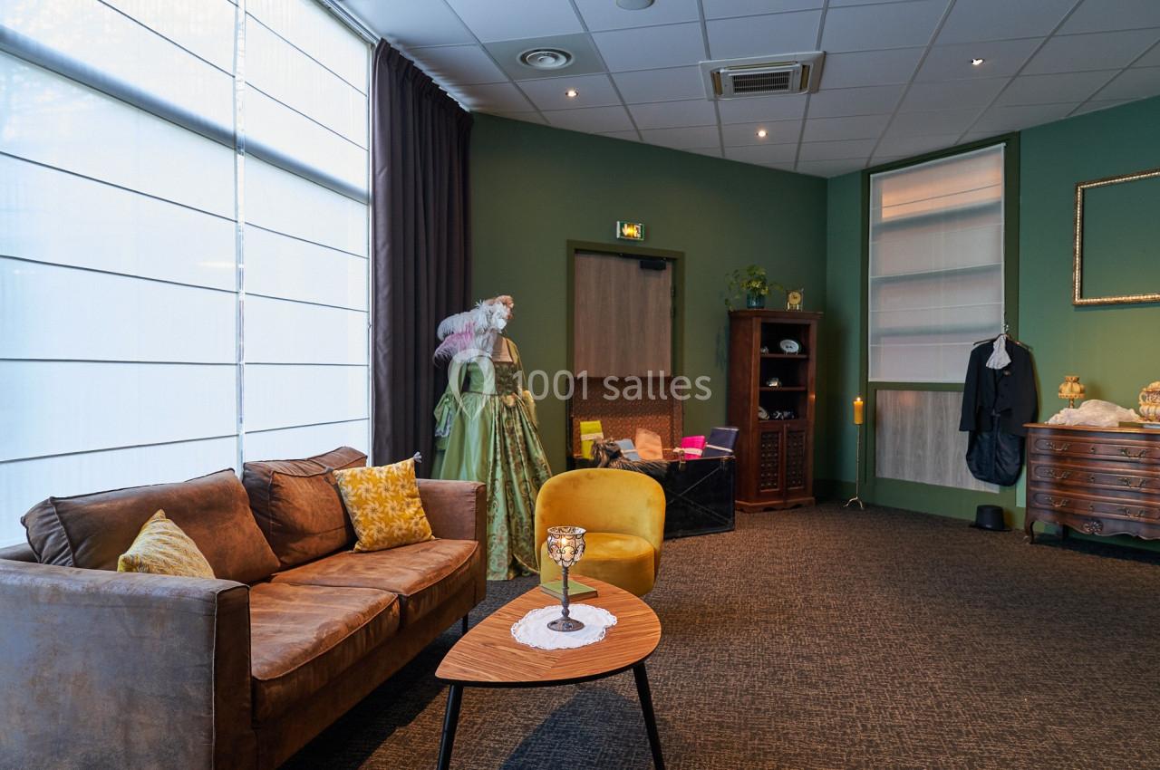 Salon aménagé avec canapé, fauteuil, table basse, armoire, et décorations, dans une pièce aux murs verts.