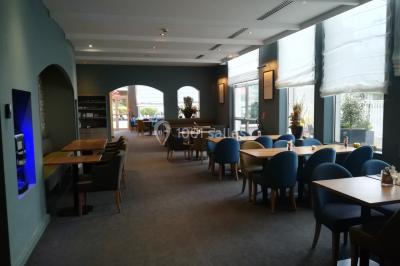Salle de restaurant lumineuse avec des tables en bois, chaises bleues et grandes fenêtres laissant entrer la lumière…