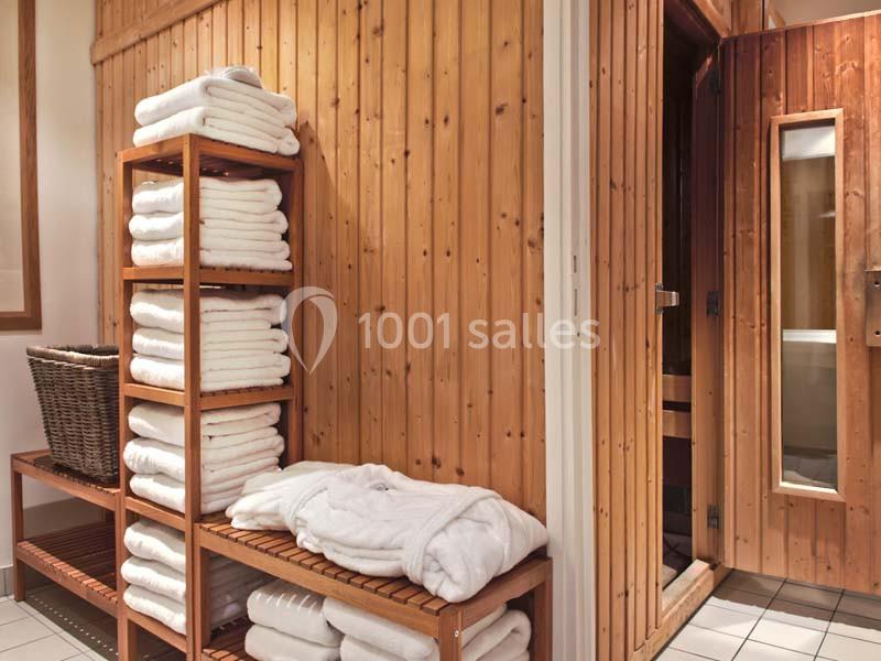 Des serviettes blanches pliées sur des étagères en bois près d'une cabine de sauna dans un espace intérieur.