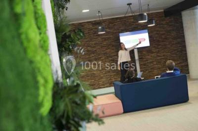 Façade vitrée d'un bâtiment moderne avec une terrasse en bois éclairée par le soleil.