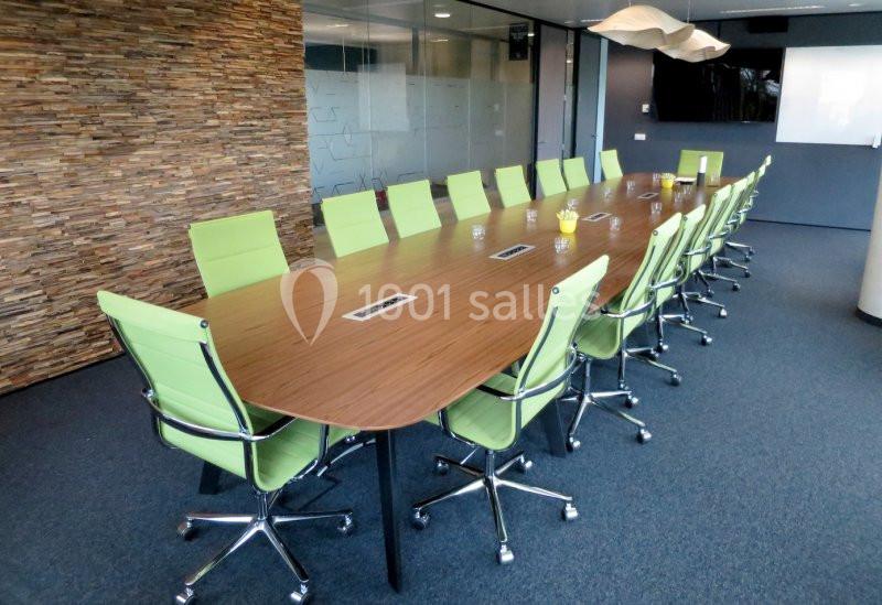 Salle de réunion avec une grande table en bois entourée de chaises vertes sur un sol en moquette bleue.