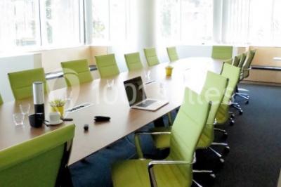 Façade vitrée d'un bâtiment moderne avec une terrasse en bois éclairée par le soleil.