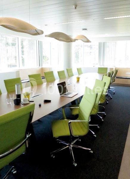 Salle de réunion lumineuse avec une grande table en bois, des chaises vertes et des fenêtres laissant entrer la lumière…